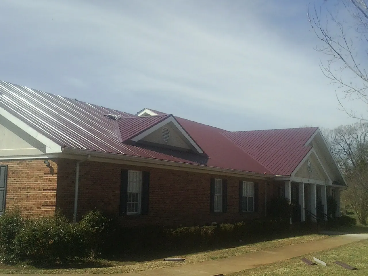 Red metal roof with gabled entries on a long brick building, from a Hail Damage Roof Repair job in South Carver