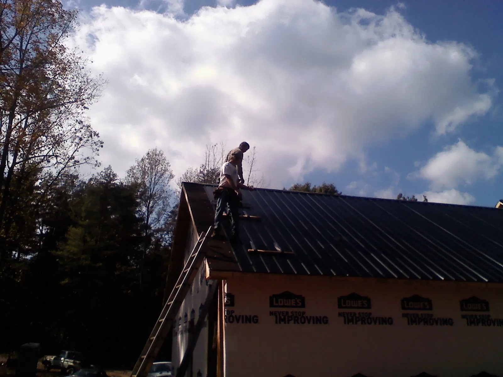Roofer fastening dark metal panels high against a cloudy sky, from a Roof Inspection job in South Carver