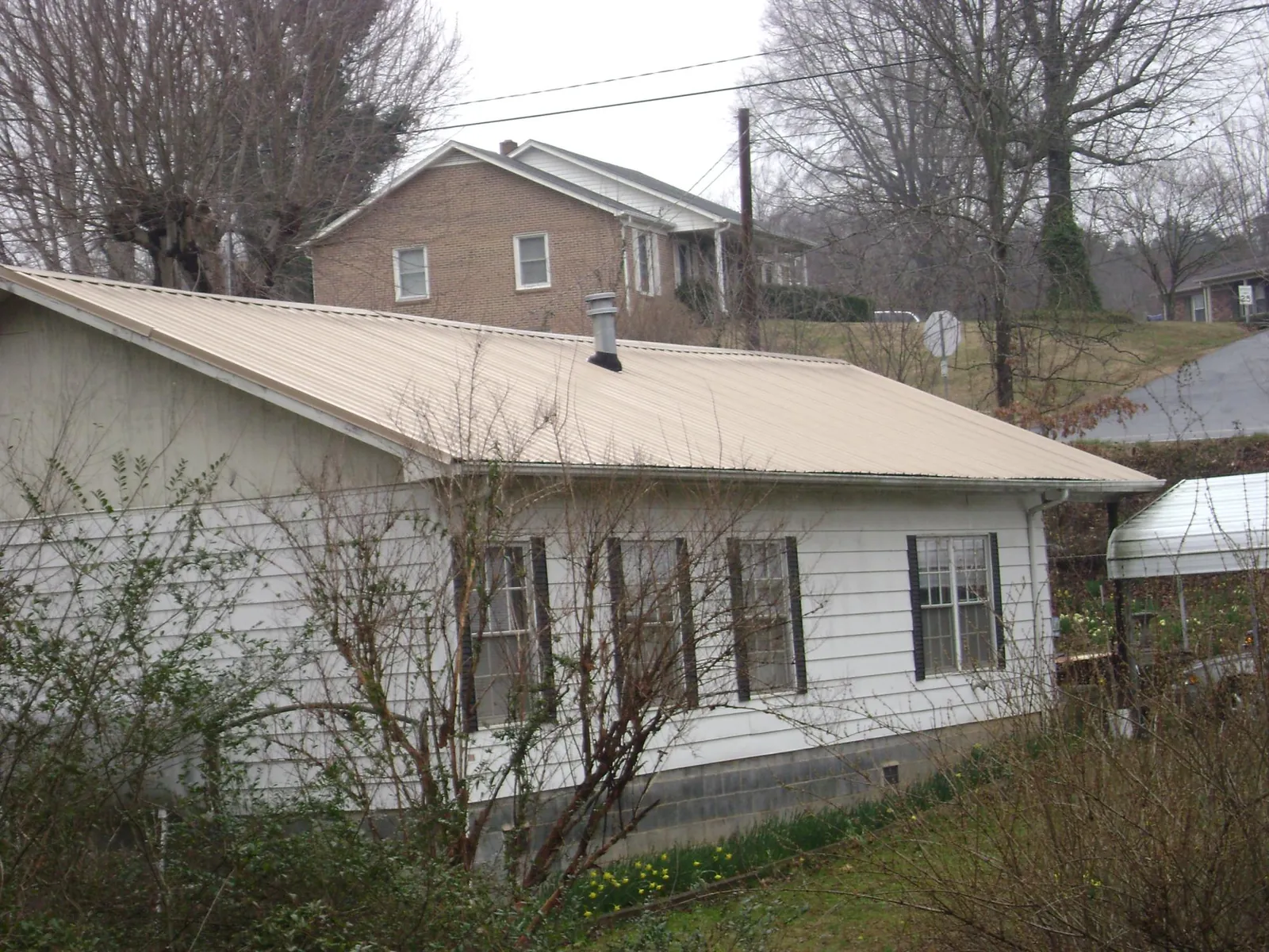 Tan metal roof on a white sided house set into a hillside — Commercial Roofing by Roofing Brothers in South Carver